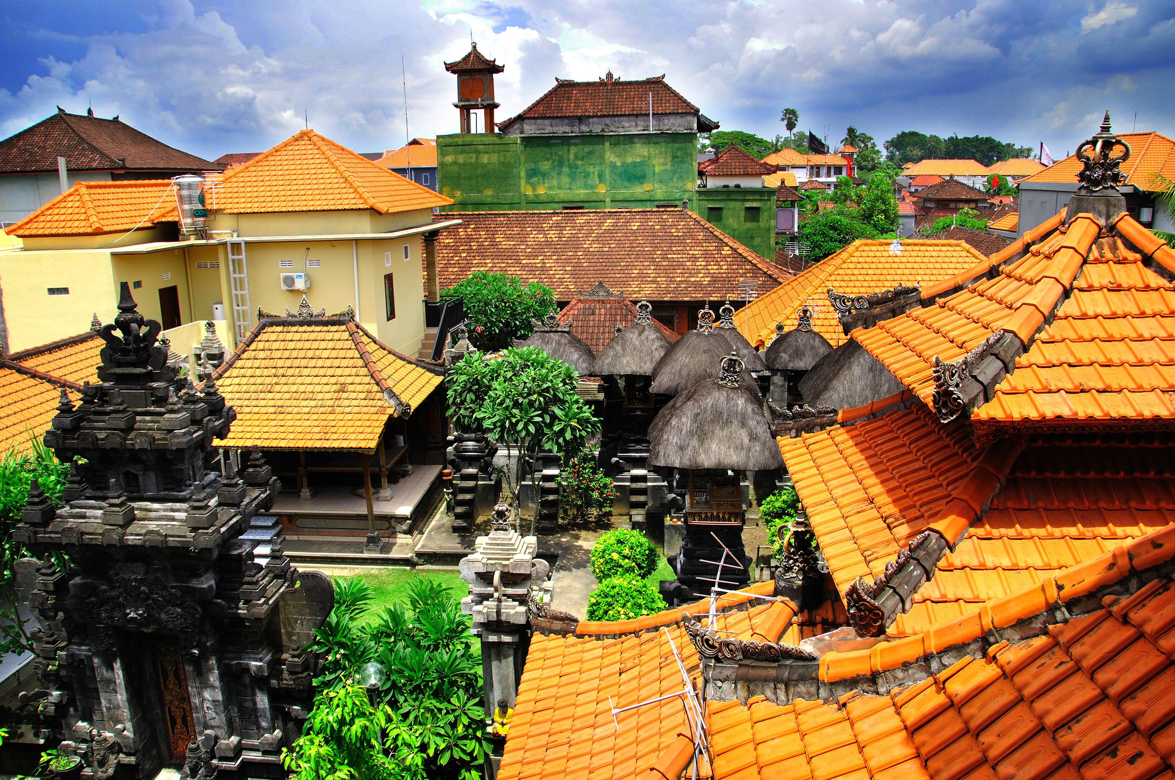 A traditional courtyard with thatched-roof buildings, a central water feature, and a bell tower.