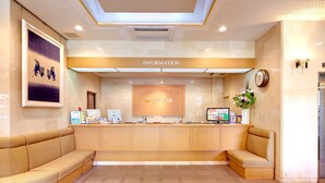A reception area with a wooden counter, a framed artwork, a clock, and a sofa. - Roco Inn Matsuyama (Naha)