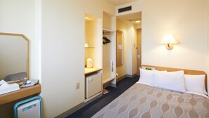 A hotel room with a bed, a desk with a lamp, a mirror, a wardrobe, and a small refrigerator. - Roco Inn Matsuyama (Naha)