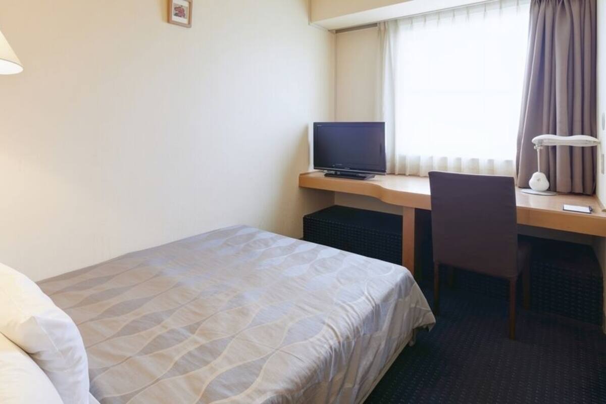 Una habitación de hotel con cama, escritorio, laptop, silla y lámpara.