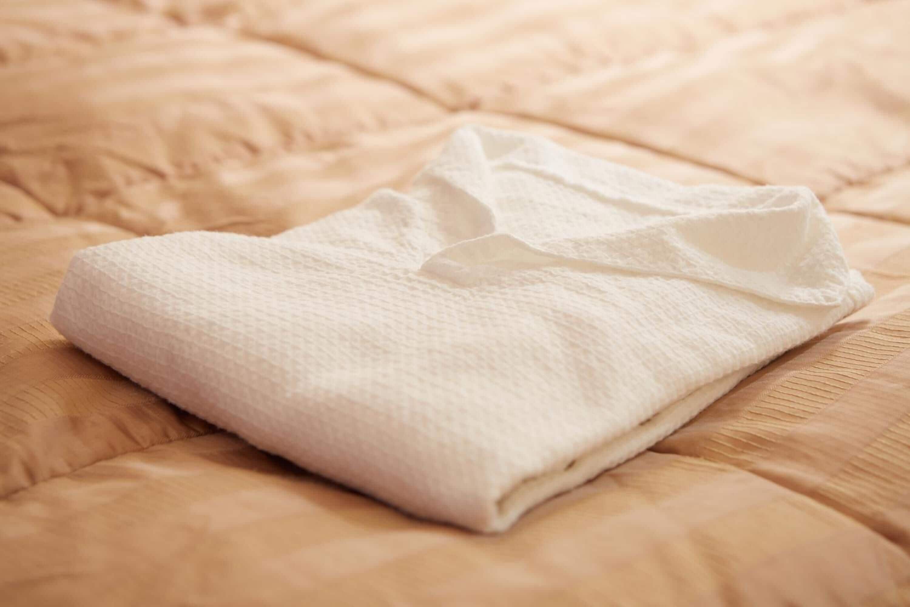 A neatly folded white towel on a textured beige bedspread.