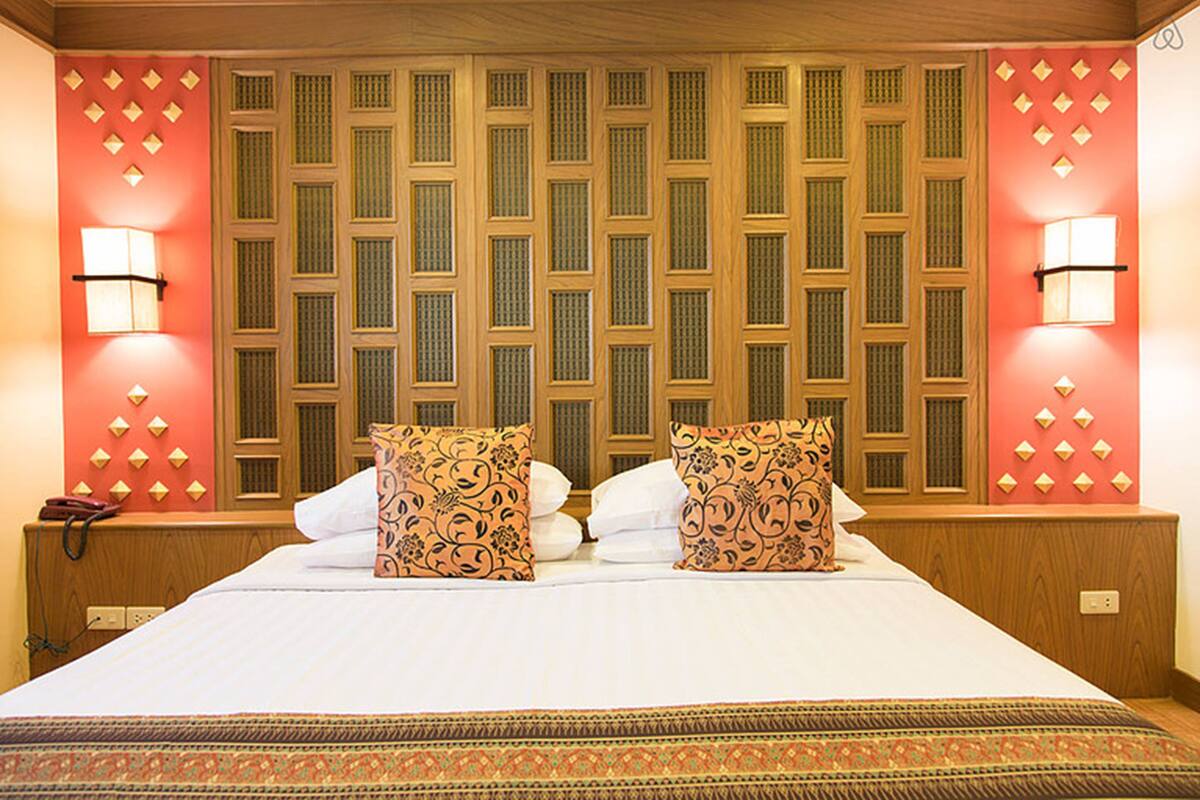 A hotel room with a large bed, patterned pillows, a wooden headboard with a geometric design, and wall-mounted lights.