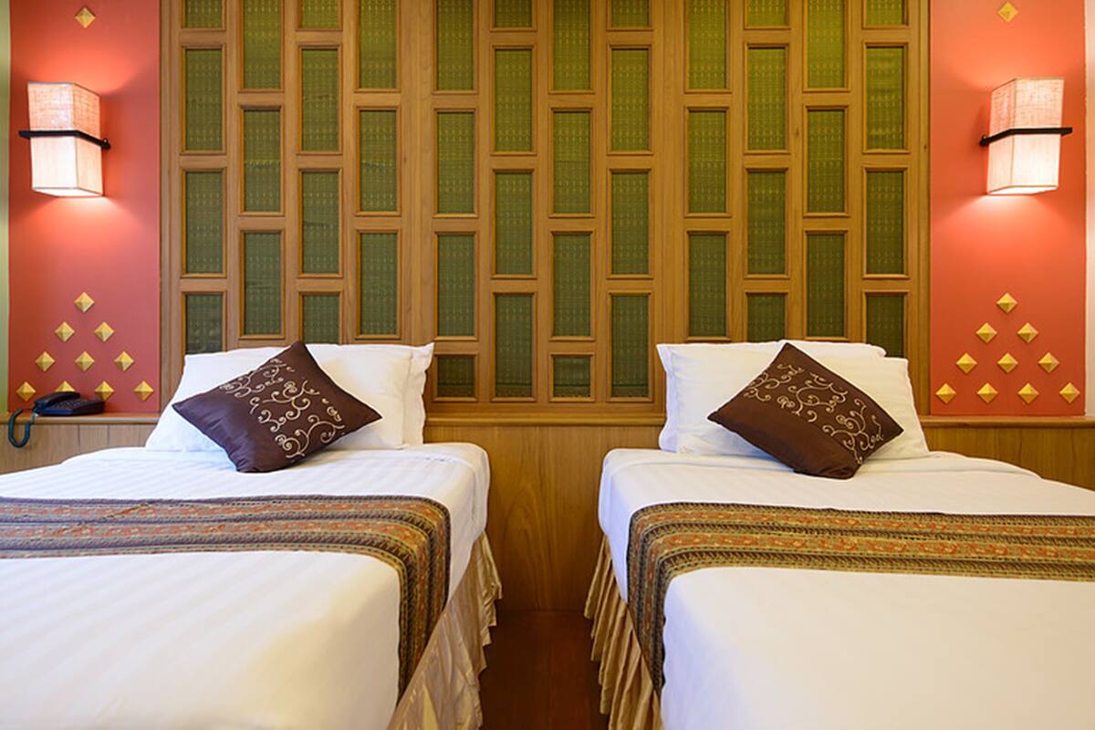 A hotel room with two beds, each with a patterned pillow, a wooden headboard, and a wall-mounted telephone.