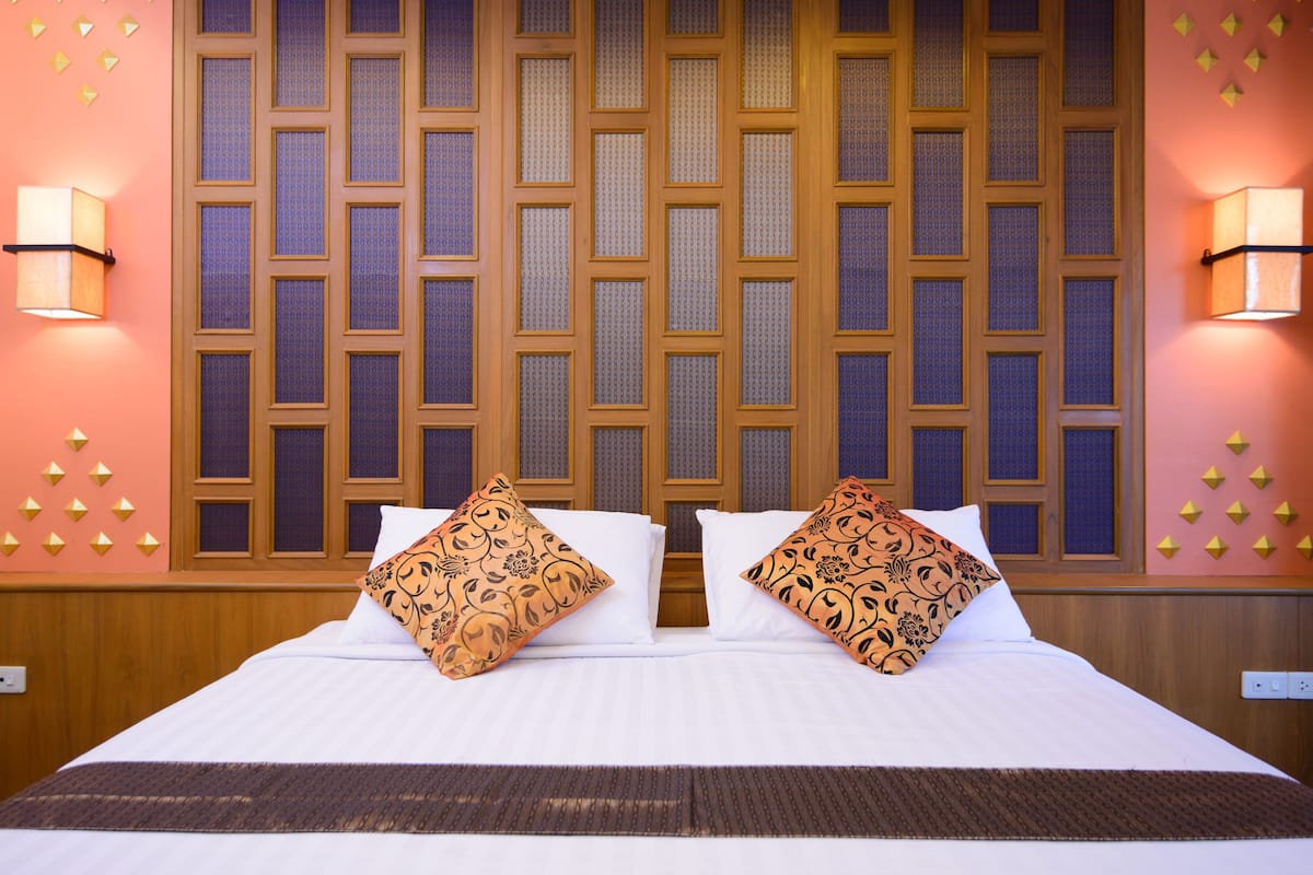 A hotel room with a large bed, two decorative pillows, a wooden headboard, and wall sconces.