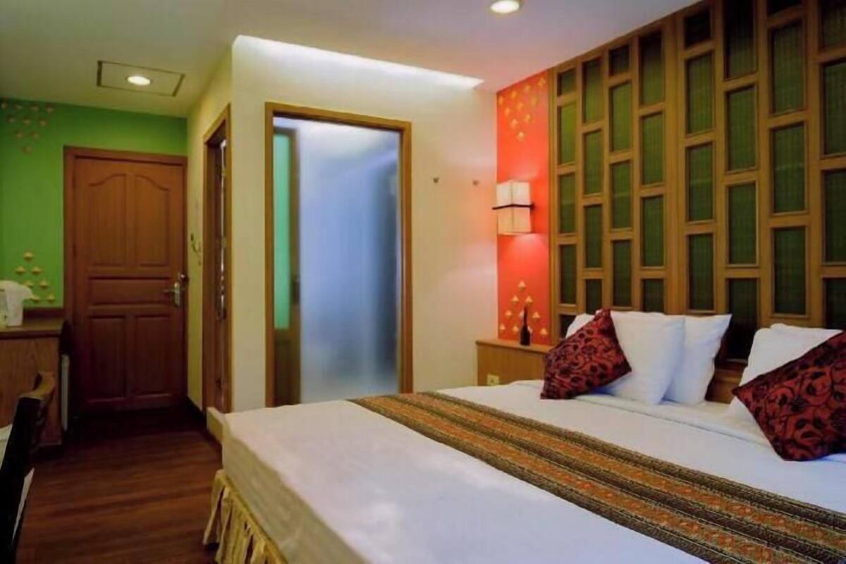 A hotel room with a bed, bedside table, lamp, and a door leading to another room.