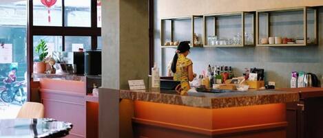A restaurant with a counter, shelves with glassware, and a potted plant.