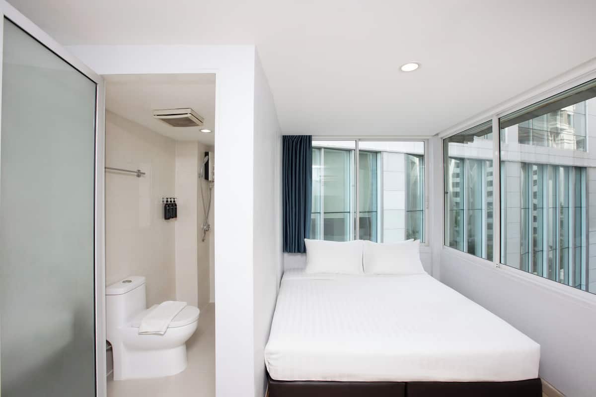 A modern hotel room with a large bed, a toilet, and a window with a view of the city.