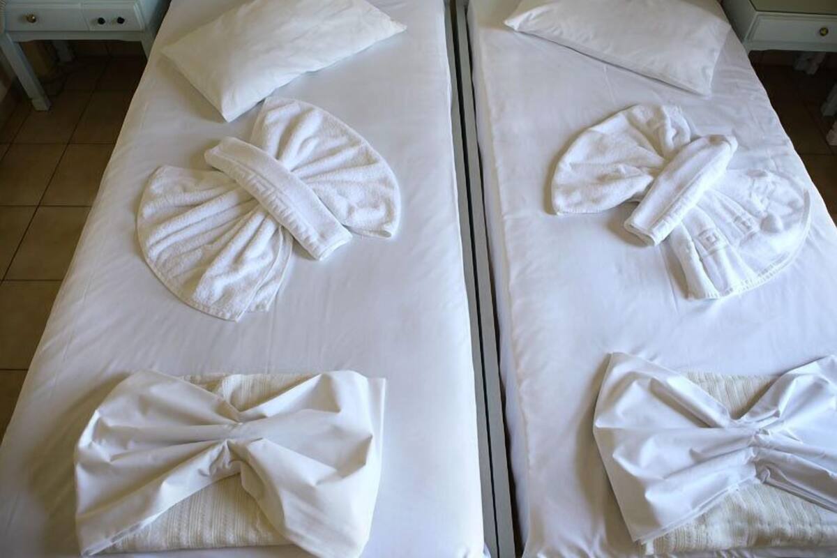 Two neatly made beds with towels arranged in a bow shape on each bed.