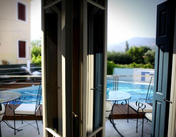 An outdoor pool area with a glass door leading to a patio with a table and chairs. - Michaelia Hotel (Lesvos)