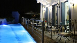 Zona de piscina exterior con barandilla, sillas y mesas.