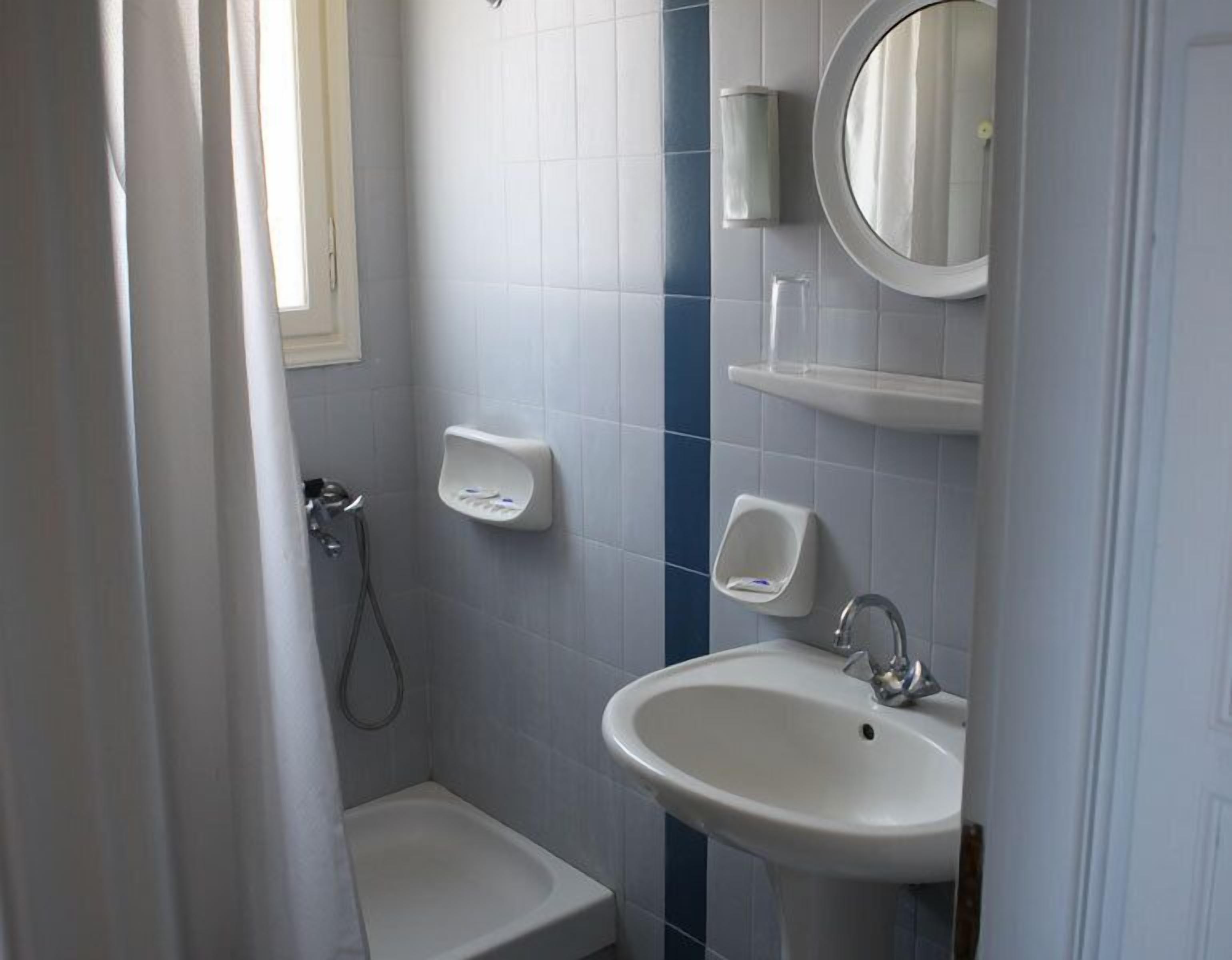 Un baño con lavamanos pedestal, ducha de mano y un inodoro pequeño.