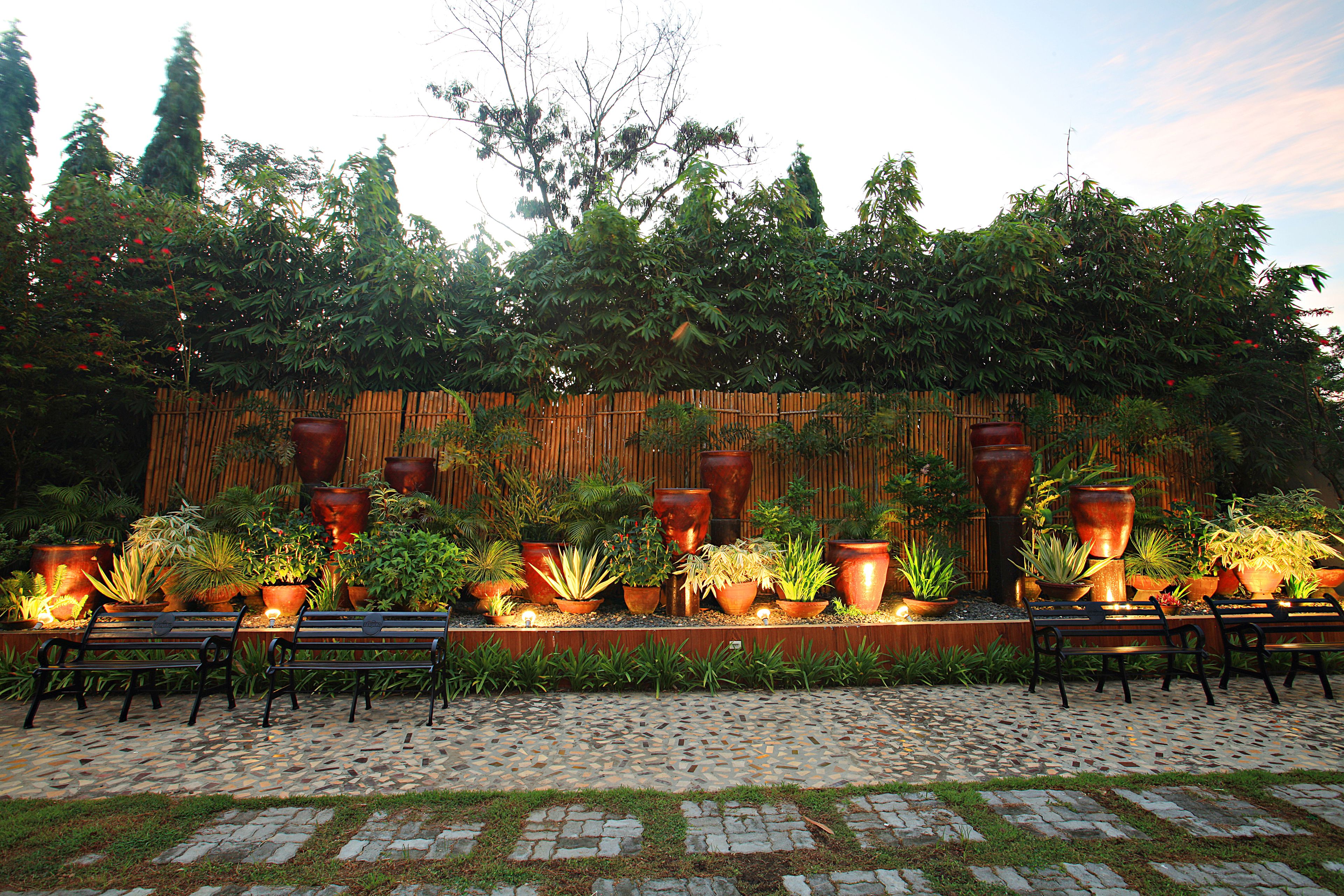 A garden patio with stone flooring, wooden benches, and large potted plants.
