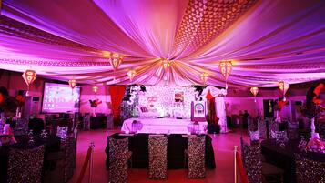 A banquet hall with tables set for a formal event, a stage with a backdrop, and a large screen.