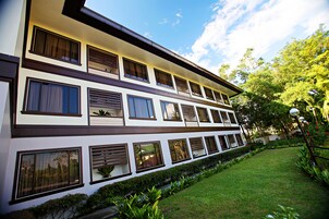 A multi-story hotel with a modern architectural design, featuring a flat roof, large windows, and a well-maintained garden.