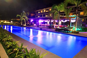 A nighttime swimming pool area with a covered seating area and palm trees.