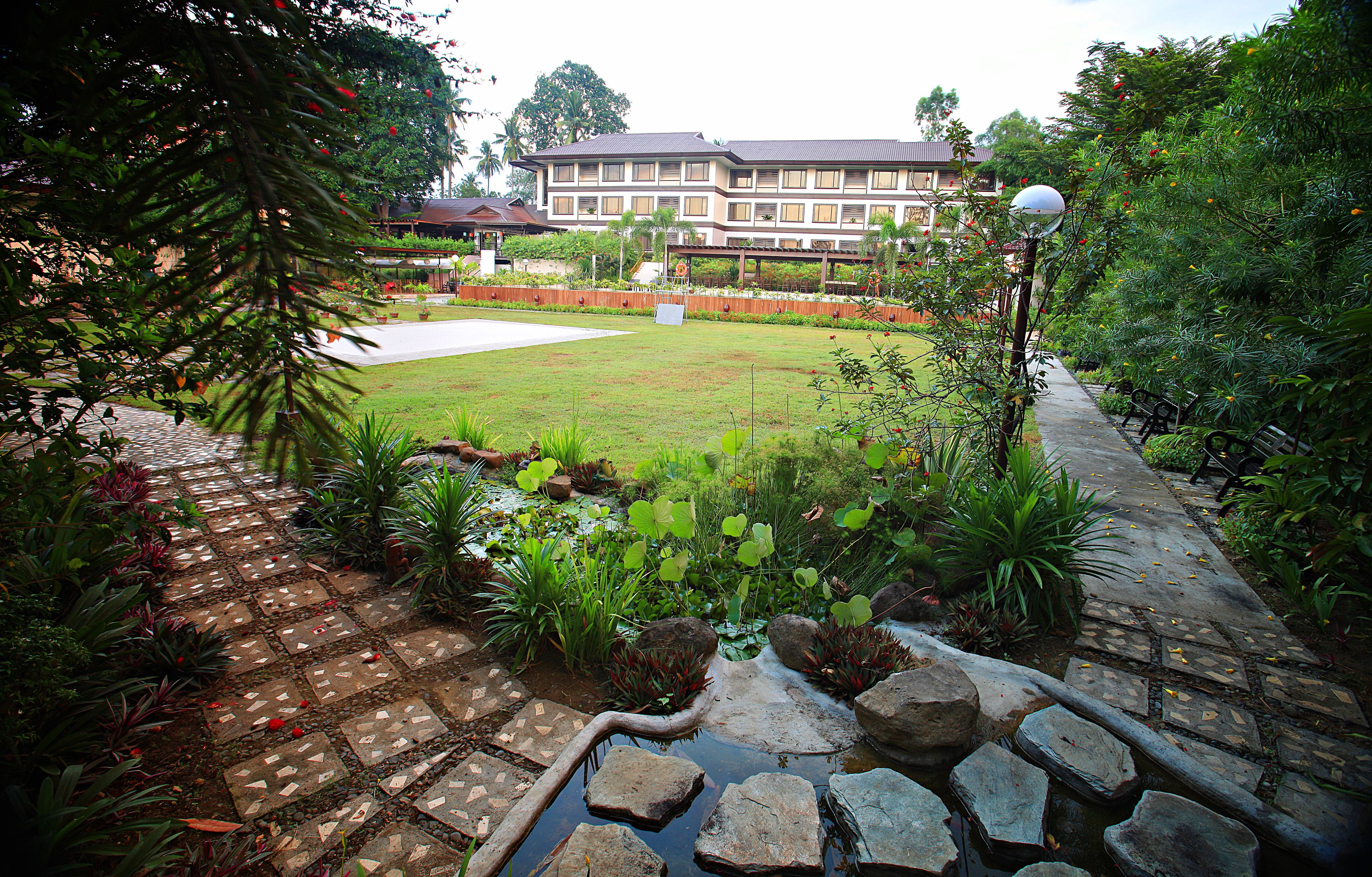 A landscaped garden with a pond, stone pathway, and a building in the background.