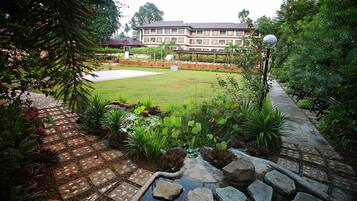 A landscaped garden with a pond, stone pathway, and a building in the background.