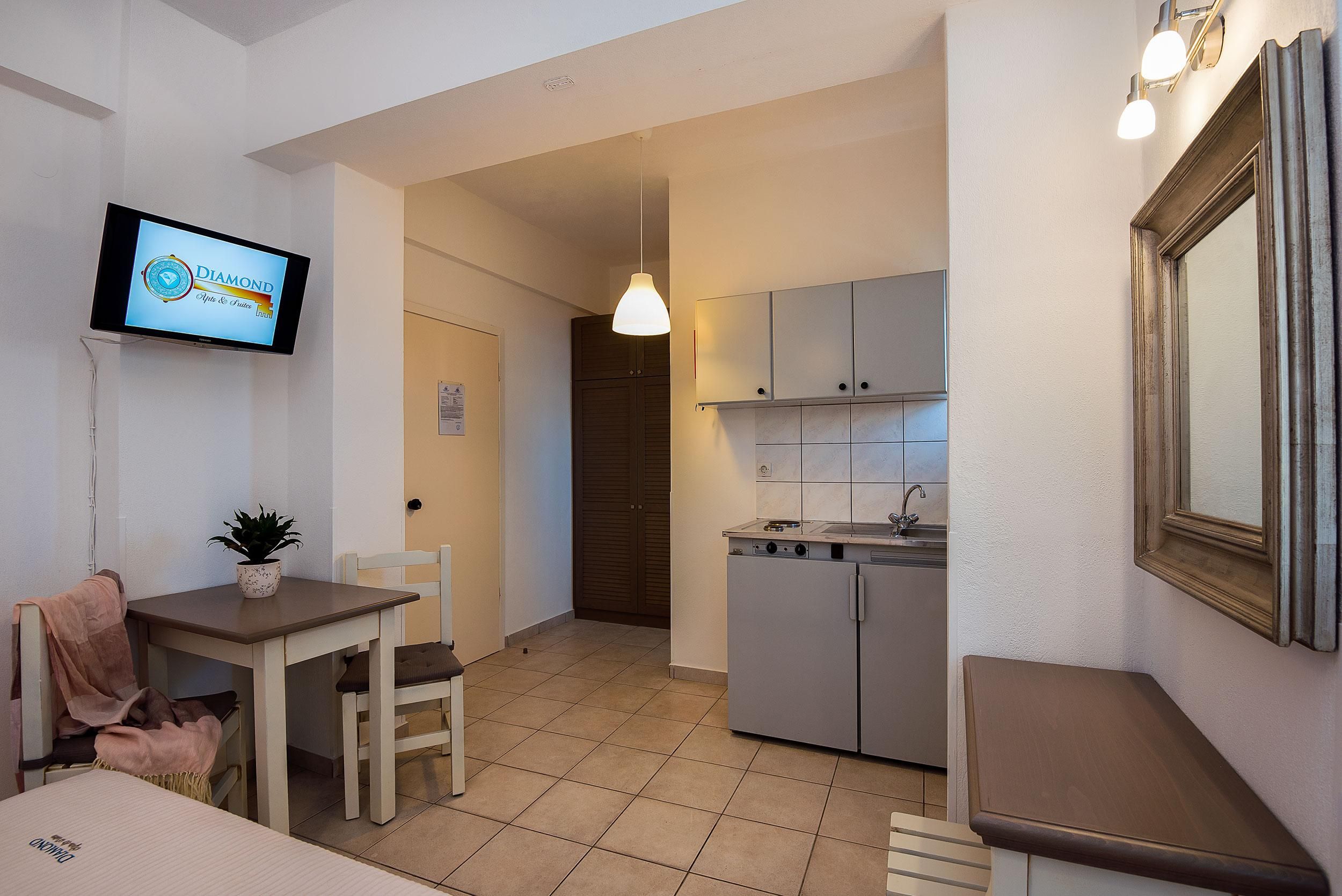 A compact kitchen with a sink, cabinets, and a television displaying 'DIAMOND' on the wall.