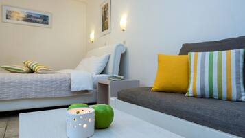 Un dormitorio moderno con cama, sofá y mesita de noche. Hay almohadas y una lámpara sobre la mesita.