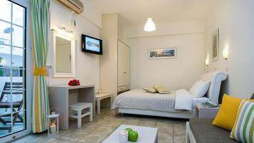 A hotel room with a bed, a desk, a chair, a table with apples and a candle, and a television on the wall.
