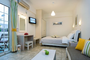 A hotel room with a bed, a desk, a chair, a table with apples and a candle, and a television on the wall. - Diamond Apts and Suites (Hersonissos)