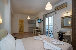 Habitación de hotel con cama, escritorio, televisor y balcón con vistas.