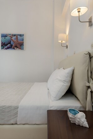A bedroom with a bed, a nightstand, a wall-mounted lamp, and a framed picture of sea creatures. - Diamond Apts and Suites (Hersonissos)