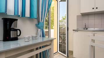 A compact kitchen with a coffee maker, two mugs, and a striped curtain.