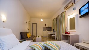 A hotel room with a bed, a small desk, a chair, a sofa, a TV, and a kitchenette. - Diamond Apts and Suites (Hersonissos)