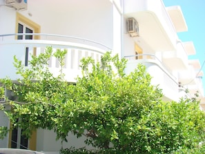 A white building with balconies and a tree in the foreground. - Diamond Apts and Suites (Hersonissos)