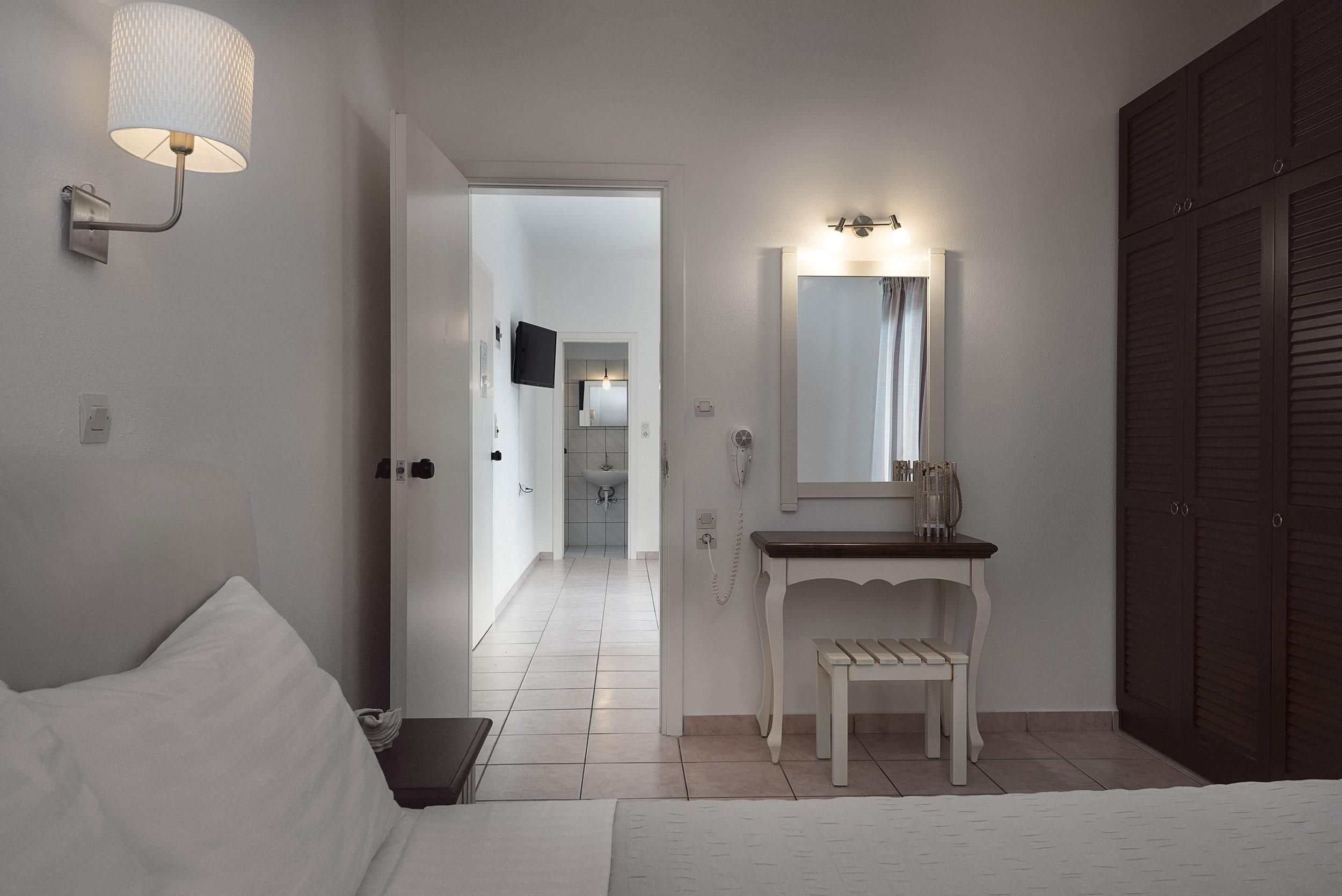Ein Hotelzimmer mit Bett, Nachttisch, Schminktisch mit Spiegel, Wandlampe und Kleiderschrank.