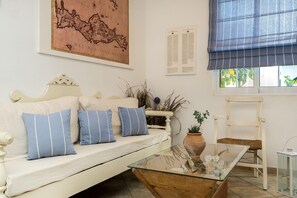 Una habitación con un sofá blanco, una mesa de centro de vidrio, un mapa en la pared, una ventana con persiana azul y una silla.