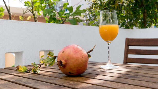 A pomegranate on a wooden table with a glass of orange juice beside it. - Diamond Apts and Suites (Hersonissos)