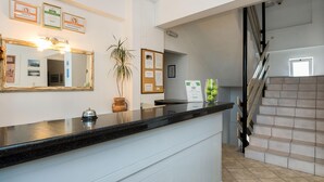 A hotel reception area with a reception desk, a mirror, framed awards, a potted plant, and a staircase. - Diamond Apts and Suites (Hersonissos)