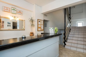 A hotel reception area with a black marble counter, framed certificates on the wall, a potted plant, and a staircase. - Diamond Apts and Suites (Hersonissos)