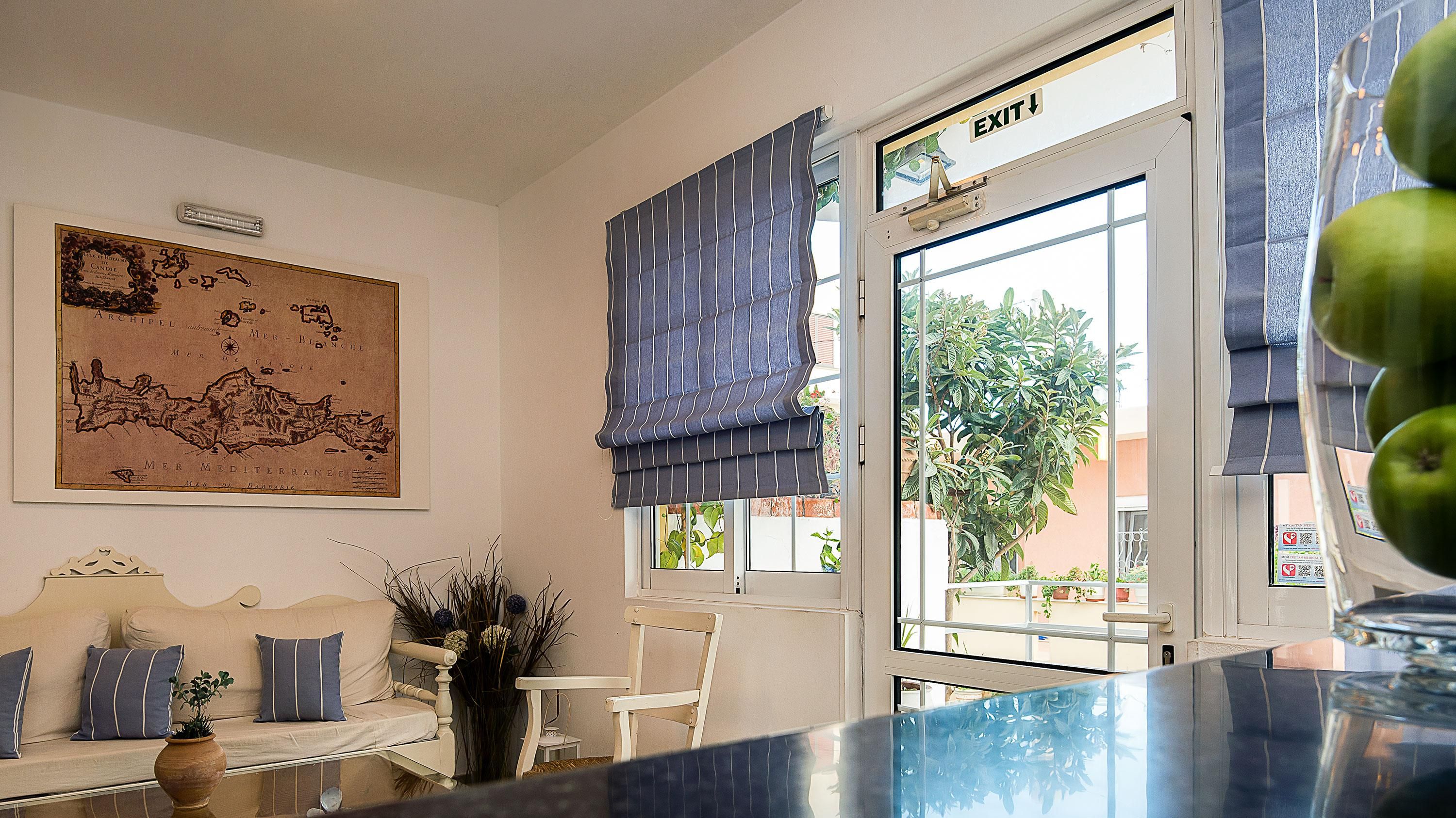 Een kamer met een kaart aan de muur, een bank, een stoel en een raam met een vluchtroutebord.