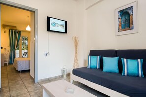 A modern hotel room with a bed, a sofa, a TV, and a framed painting. - Diamond Apts and Suites (Hersonissos)