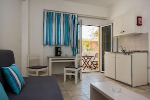 A compact living space with a kitchenette, a dining area, and a sofa with a striped pillow. - Diamond Apts and Suites (Hersonissos)