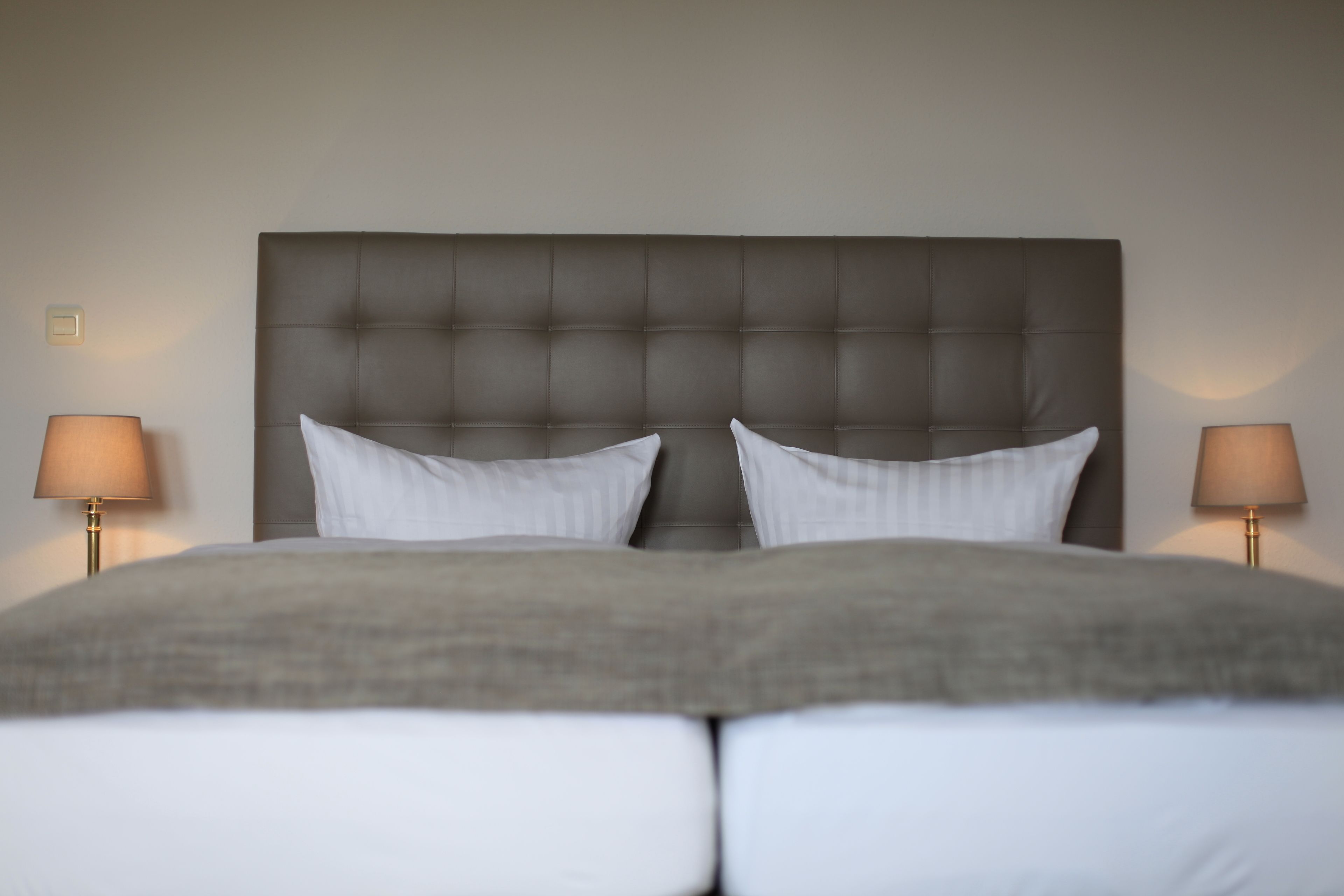 A neatly made bed with a tufted headboard, two bedside lamps, and a neutral-toned wall.