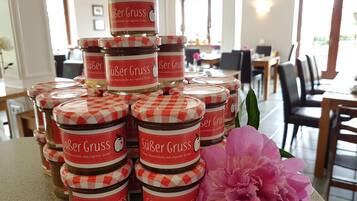 A stack of jars labeled 'Süer Gruss' with a checkered lid design, placed on a table with a pink flower beside them.
