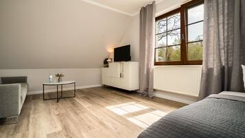 A bedroom with a bed, a TV on a cabinet, a small table with a lamp, and a window with curtains.