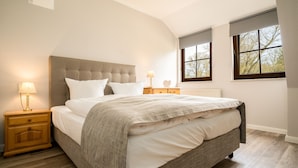 Een slaapkamer met een groot bed, twee nachtkastjes en een raam met uitzicht op bomen.