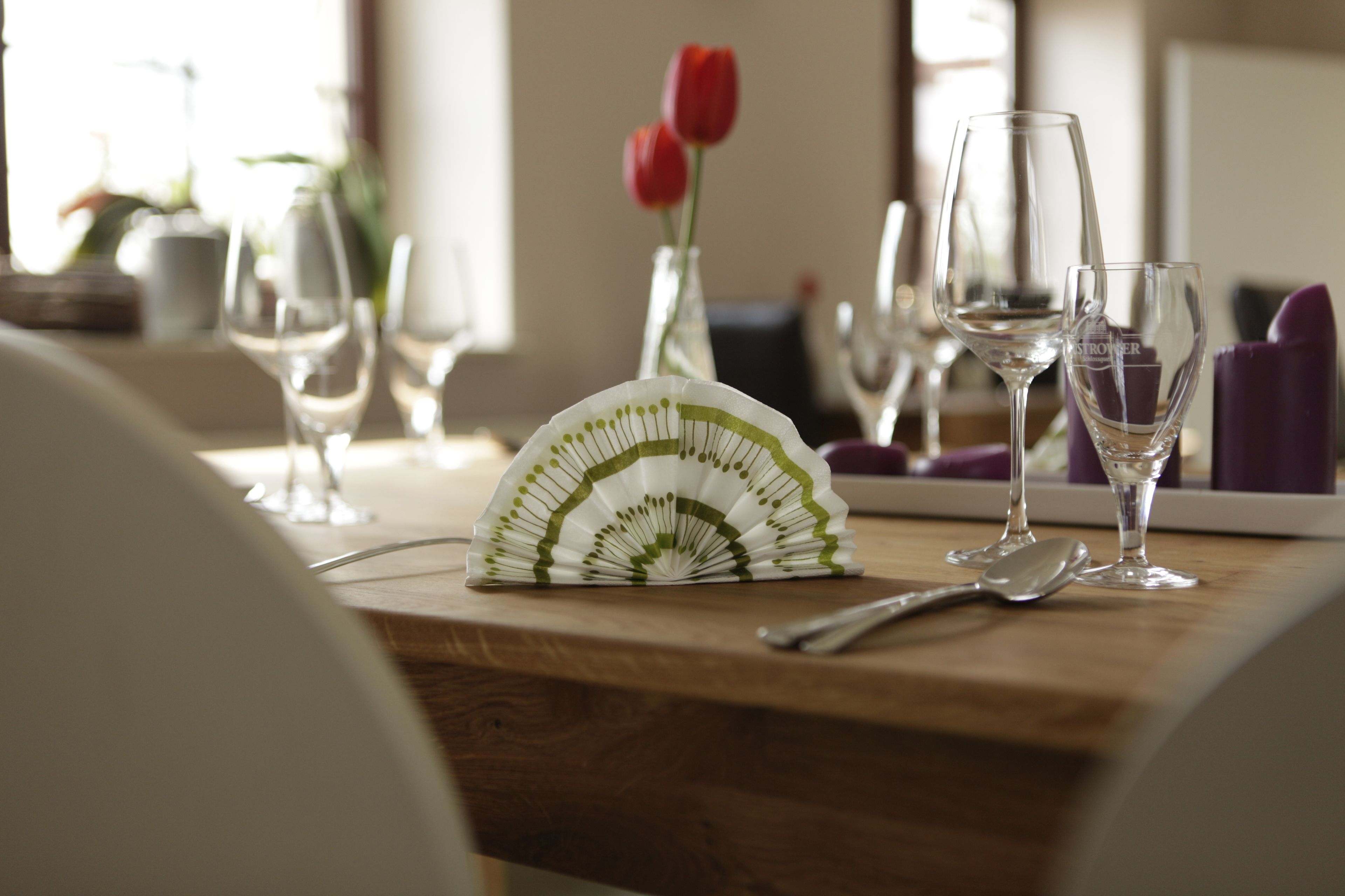A dining table with a fan, wine glasses, and a vase with red tulips.