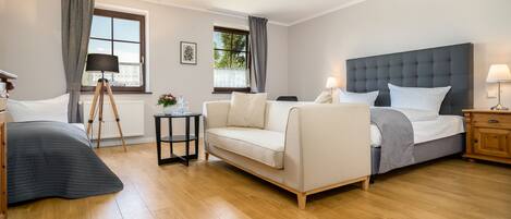 A hotel room with a bed, a sofa, a desk, and a window with curtains.