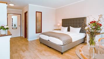 A modern hotel room with a large bed, a bedside table, a lamp, and a vase with flowers.