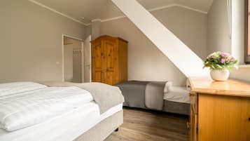 Un dormitorio con dos camas, un armario de madera y una mesita con un florero.
