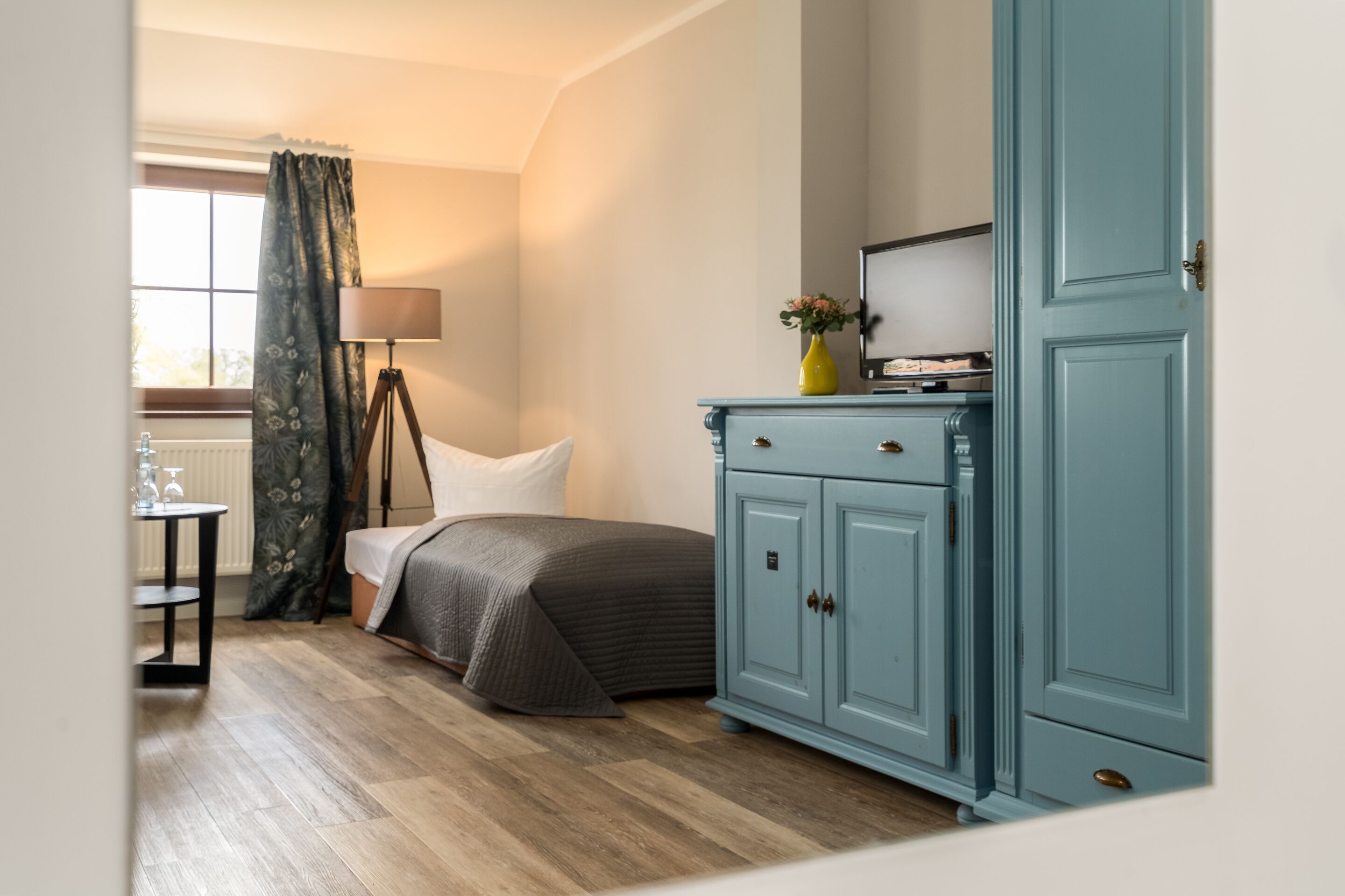 A bedroom with a bed, a nightstand, a lamp, a dresser, and a window with curtains.
