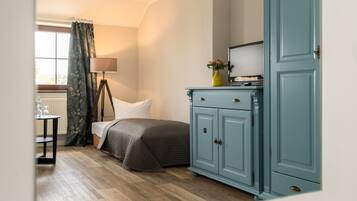 A bedroom with a bed, a nightstand, a lamp, a dresser, and a window with curtains.