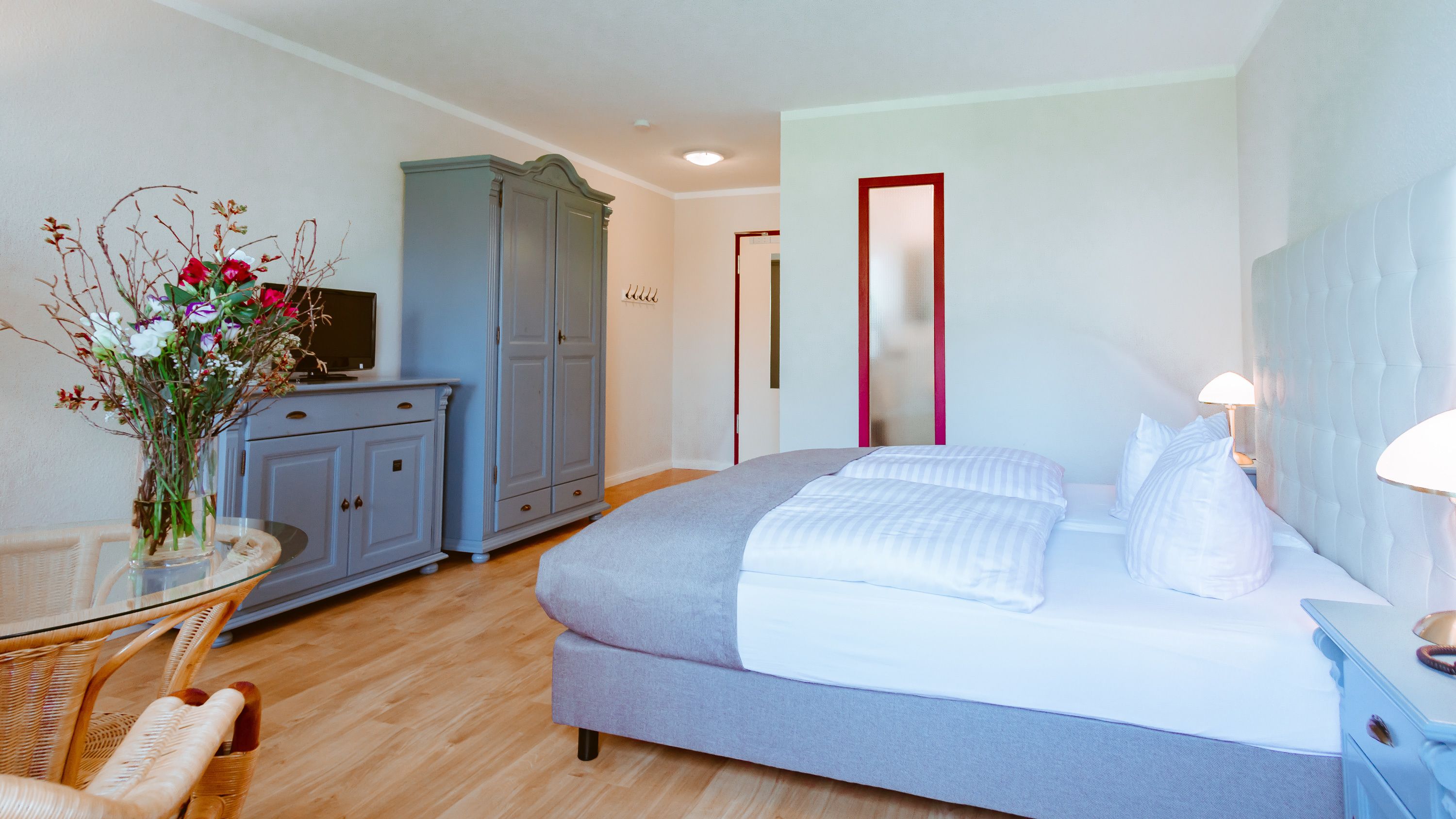 Un dormitorio con cama, armario, escritorio con silla y un jarrón de flores.