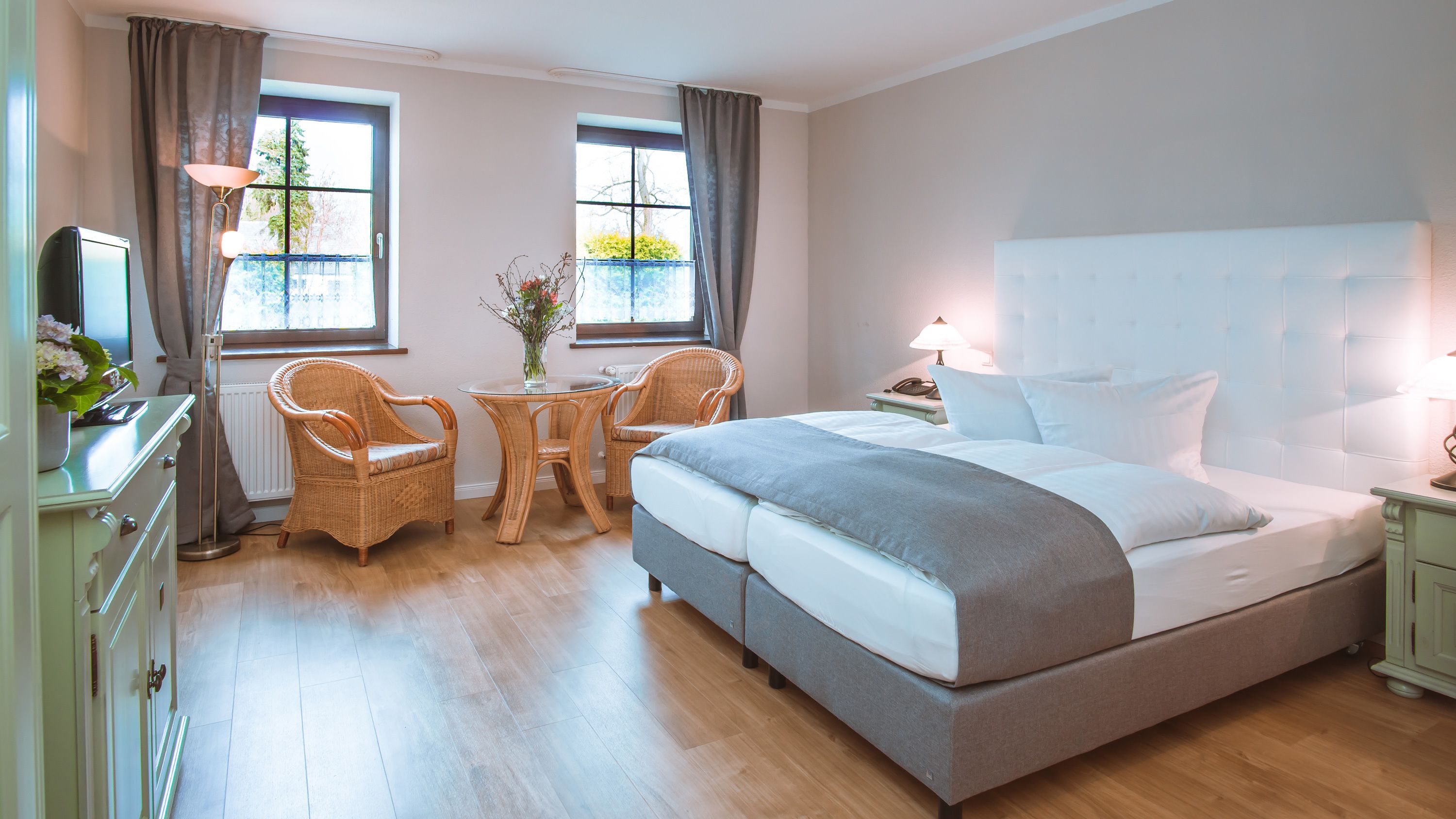 Habitación de hotel con una cama grande, dos sillas de mimbre, una mesita y un escritorio con lámpara.